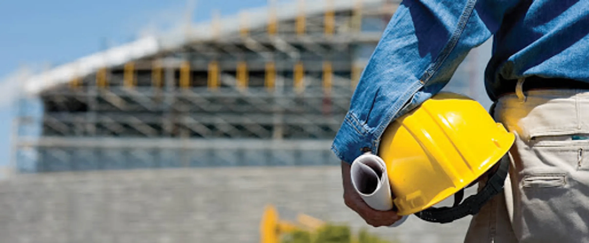 Contractor on site holding a hard hat in front of a building under construction