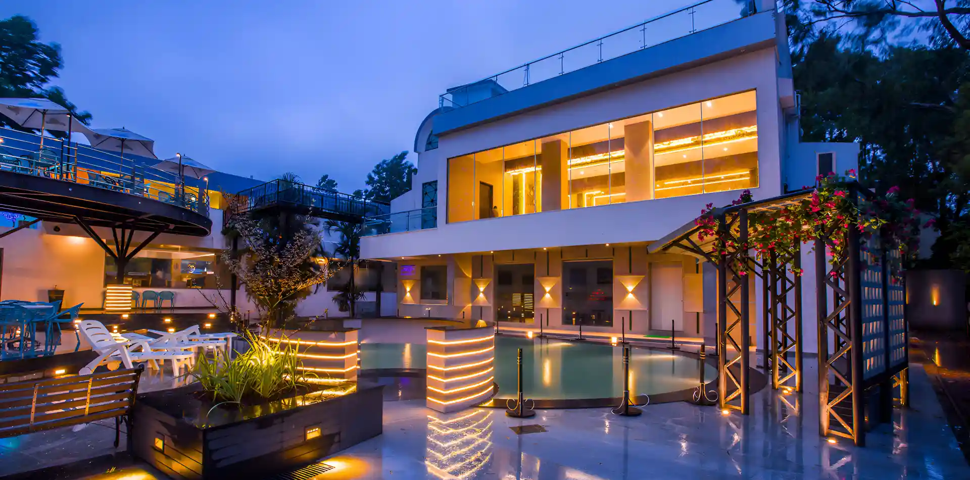 Modern hospitality-style villa exterior with lighting and pool area at dusk